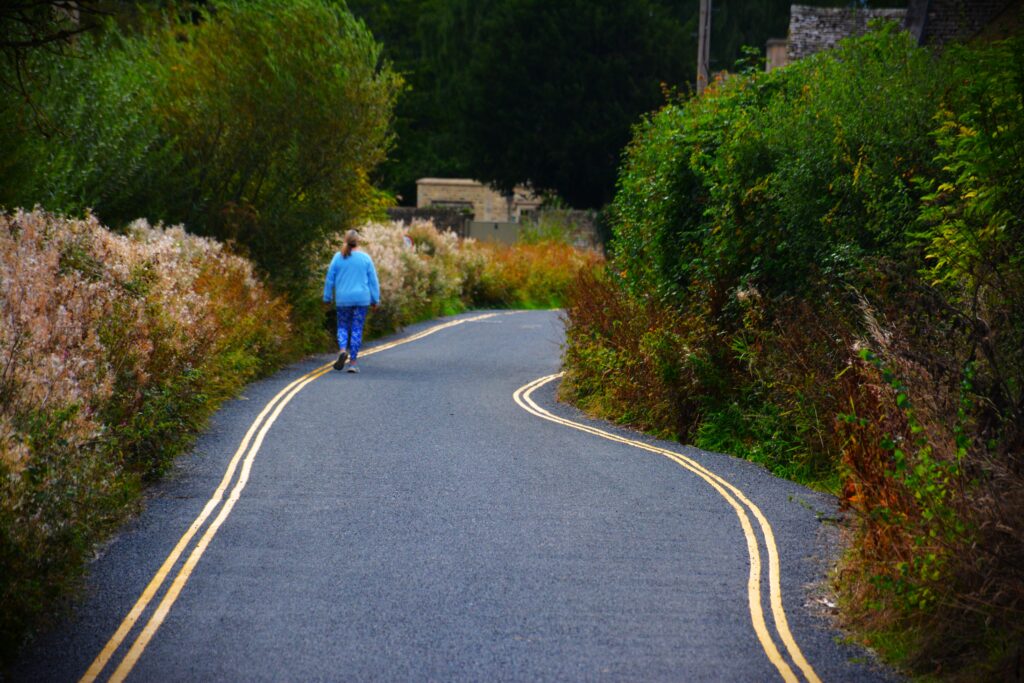 Lady walking down solitary road in Lower Slaughter, Cotswolds England
